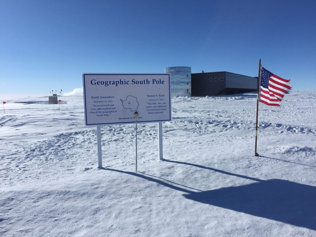 Знак Geographic South Pole и флаг у станции Амундсен-Скотт